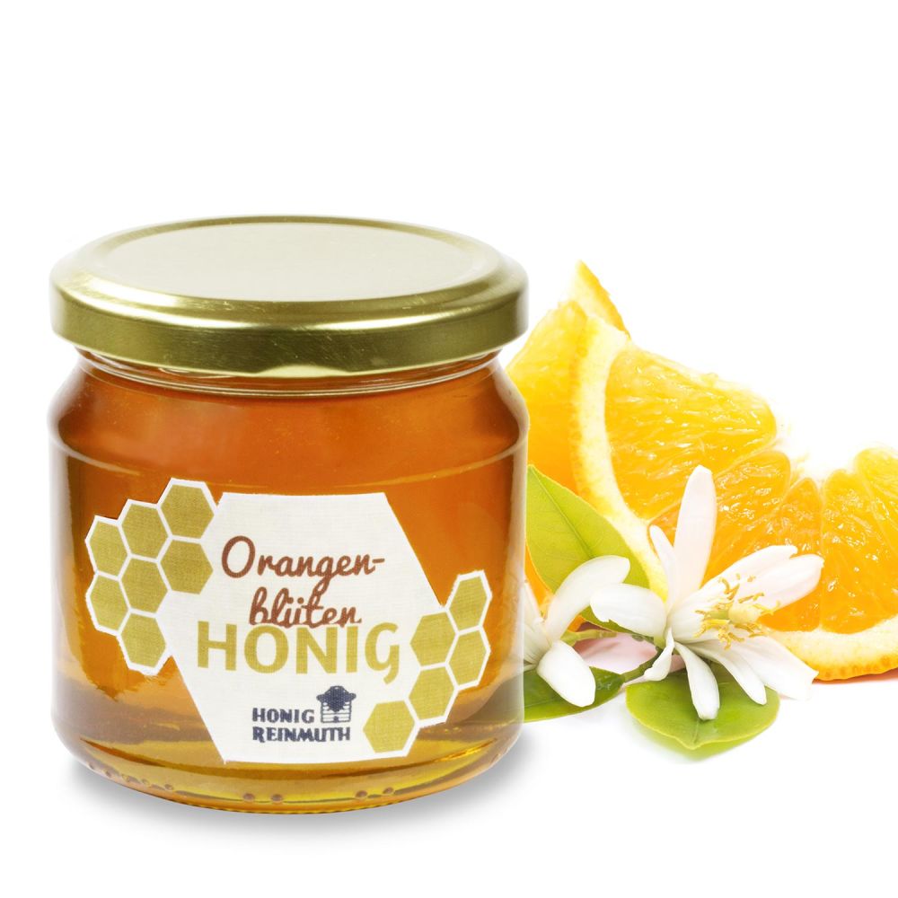 Orangenblütenhonig im Glas vor Orangenblüten und Orangenscheiben