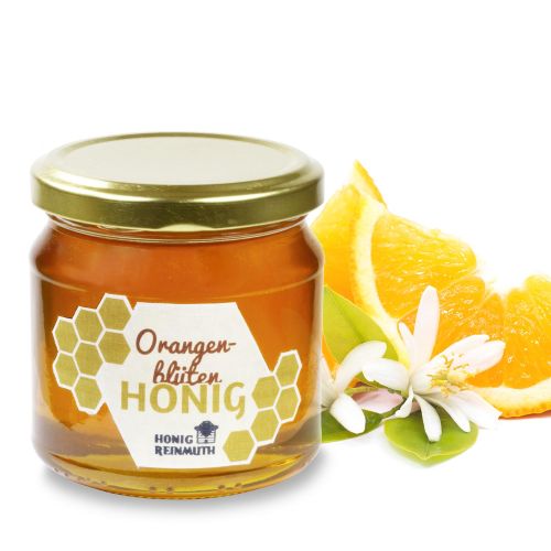 Orangenblütenhonig im Glas vor Orangenblüten und Orangenscheiben